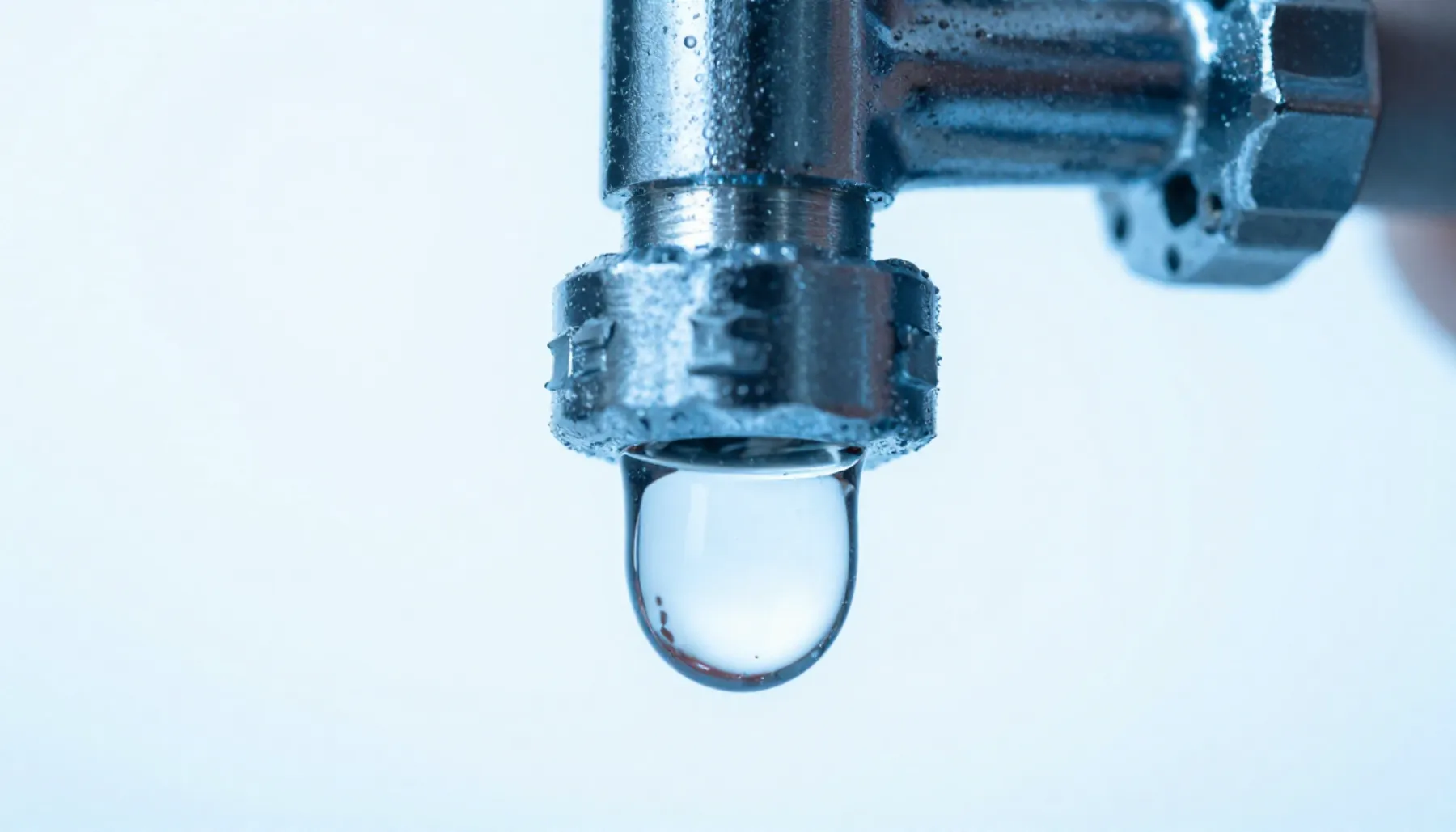 Ilustración: gota de agua que cuelga de una conexión cromada.